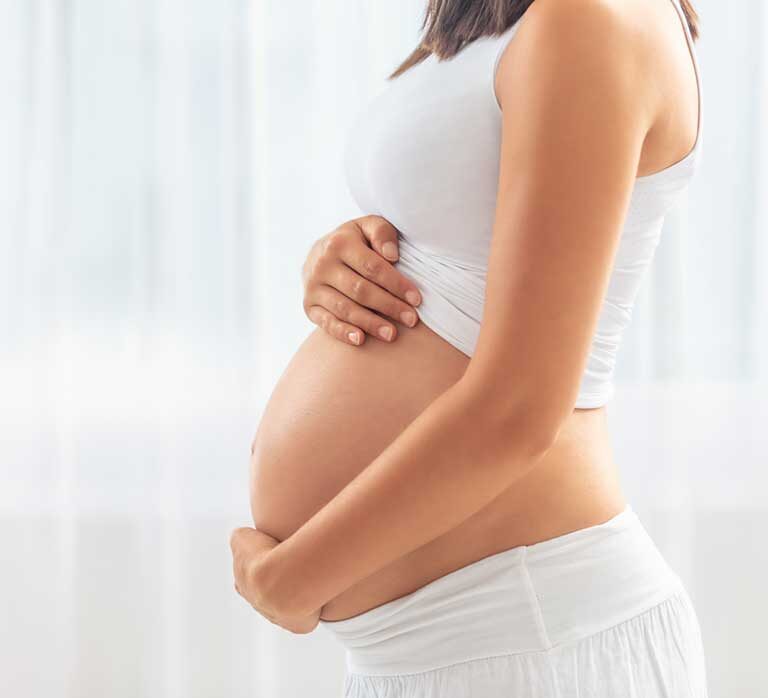 A pregnant woman wraps her arms around her torso