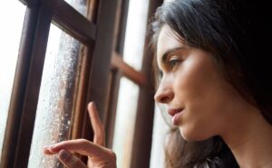 A woman looks out a window covered in raindrops.