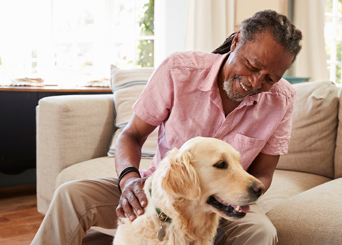 An elderly African American man smiles as he pets a golden retriever.