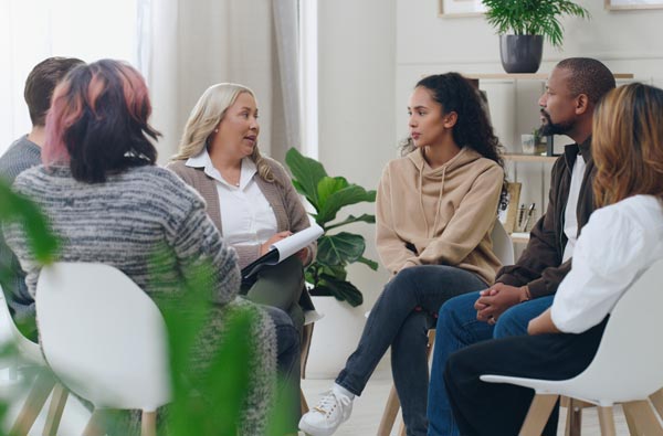 A diverse group of people sit together during a talk therapy group session.