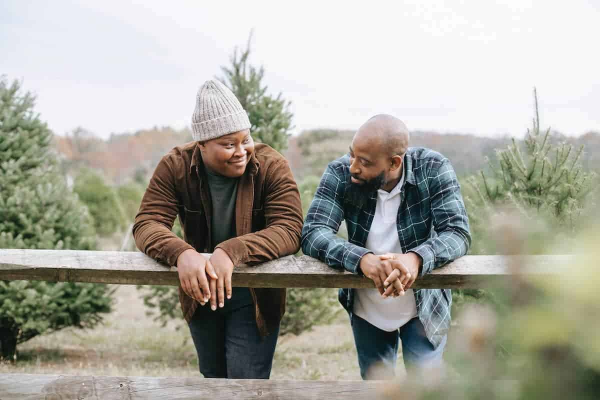 Two men lean over a fence post at a Christmas tree farm.
