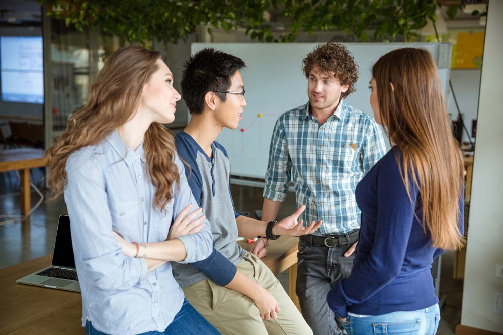 A group of two girls and two boys have a discussion in a classroom setting.